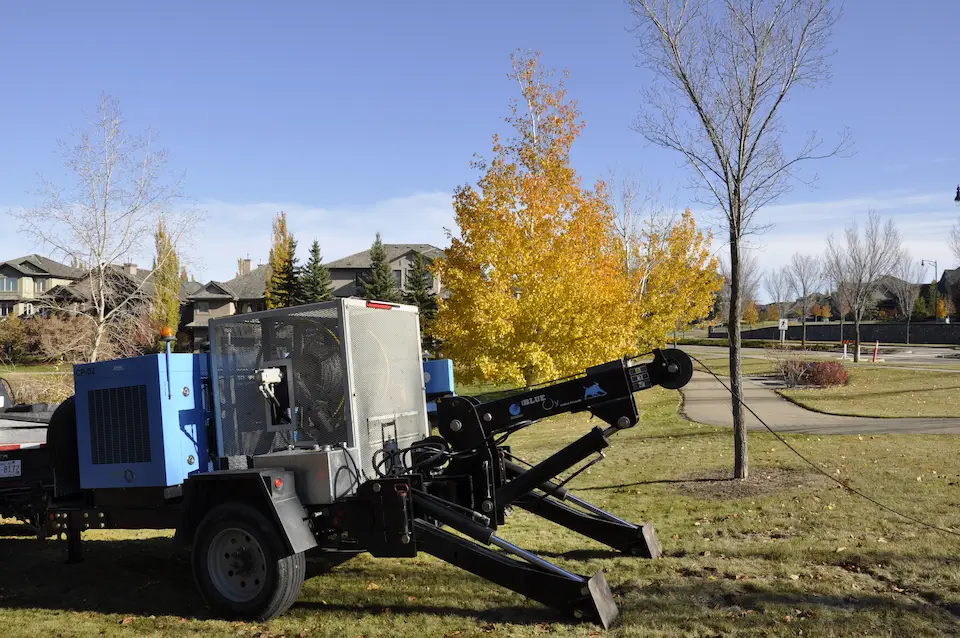 A cable pulling machine sitting in front of yellow fall trees.