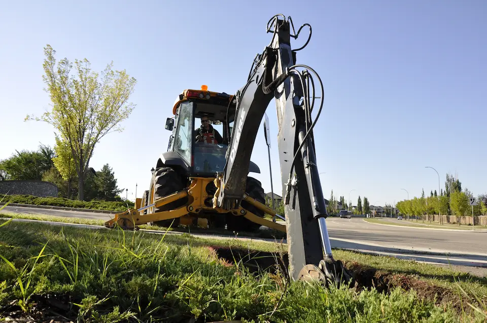 A low angle shot of an excavator with it's stabilizers in place, digging a hole.