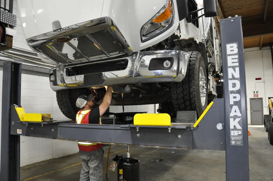 A mechanic wearing safety gear working on a 5 ton truck on a lift.