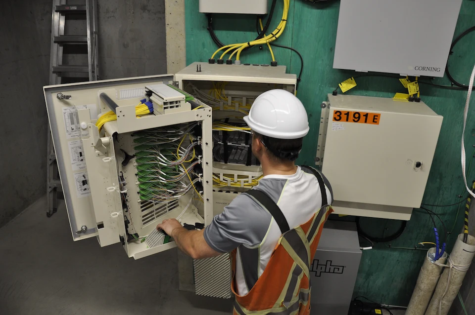 An employee wearing safety gear interacting with a panel with a large number of clear cables running into it.